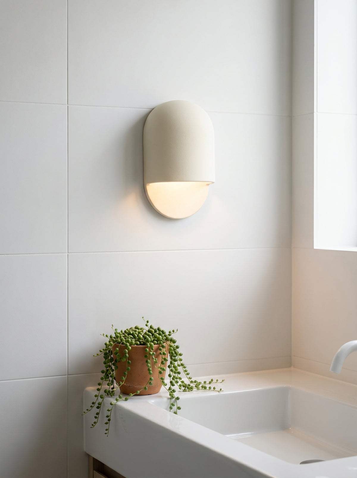 White ceramic wall sconce AX472 lit above a bathroom sink, damp-rated for bathroom use