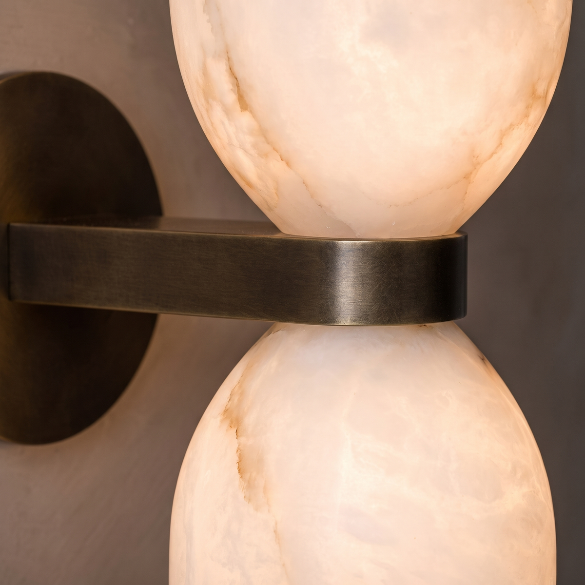 Close-up of illuminated alabaster shades and bronze band on double wall sconce