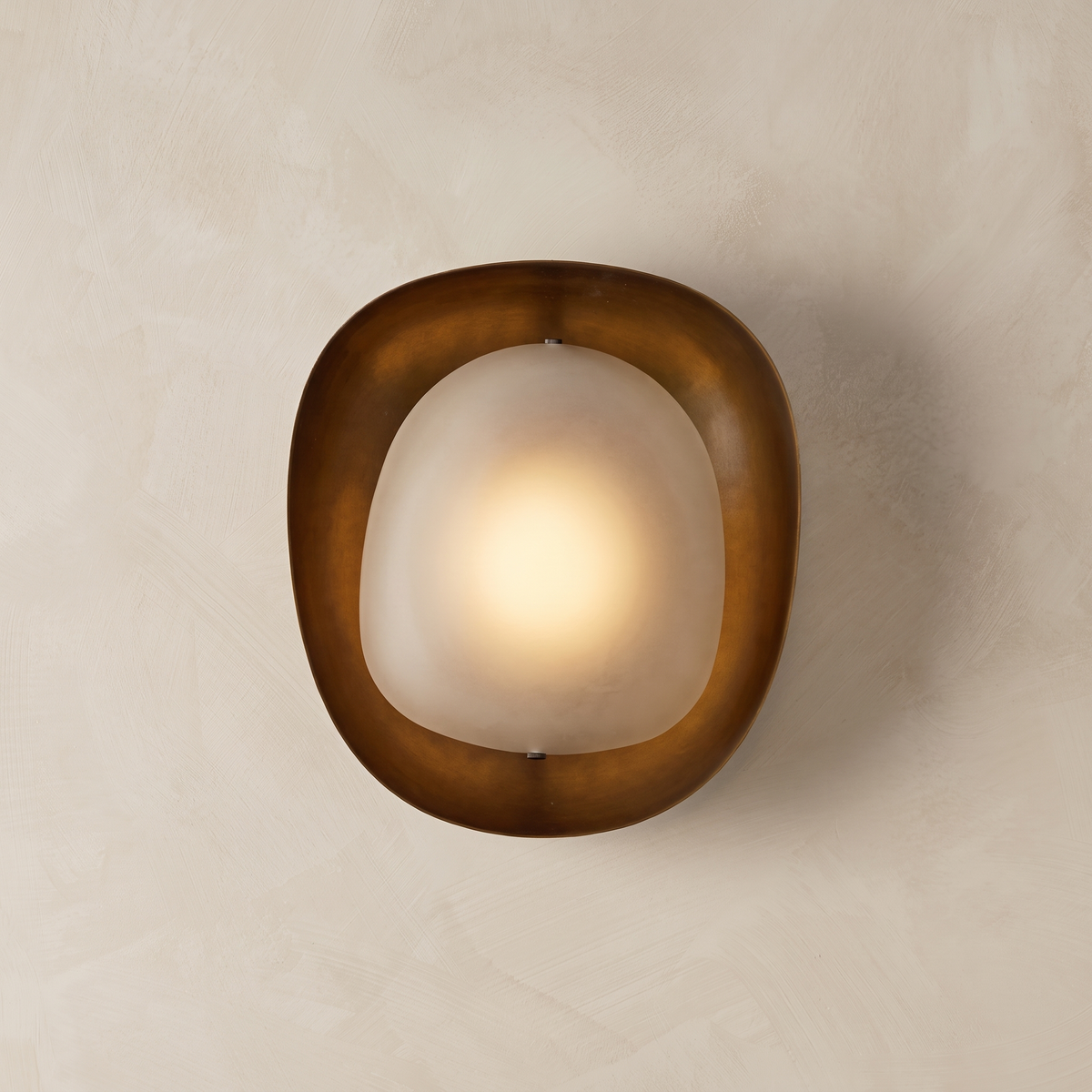 AX924 sculptural bronze wall sconce lit – hand-finished bronze ring with glowing frosted glass diffuser on plaster wall