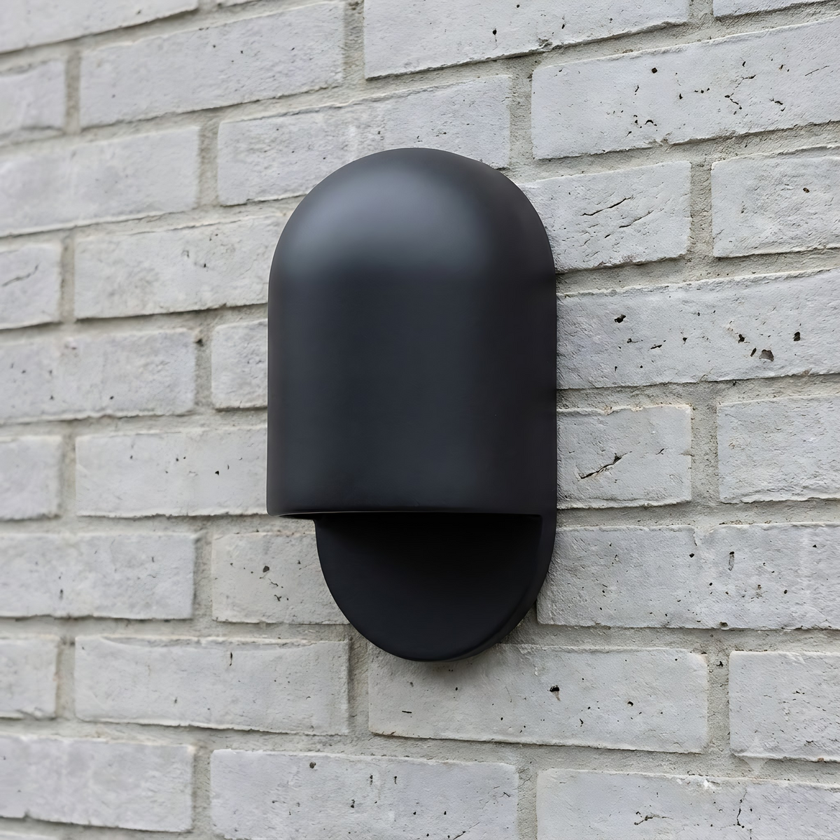 AX472 black ceramic outdoor wall sconce, unlit, on a white-painted brick exterior wall